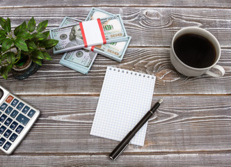 A notebook with a blank page, coffee, a calculator, a bundle of money a dollar, a plant. Concept business with copy space for any design. office table. Book-keeping equipment