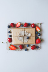 Naklejka na ściany i meble Cute gift box wrapped with craft paper and summer berries top view. Summer gift