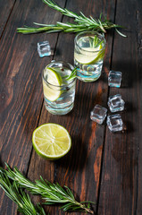Alcoholic drink - gin tonic cocktail - with lime, rosemary and ice on rustic wooden