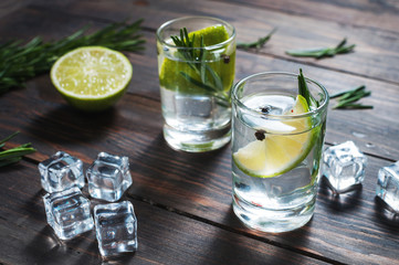 Alcoholic drink - gin tonic cocktail - with lime, rosemary and ice on rustic wooden table