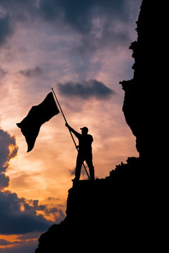 Silhouette of a man on top of a mountain with a national flag of victory! The idea: patriotism, sport victory, business success.