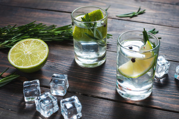 Alcoholic drink - gin tonic cocktail - with lime, rosemary and ice on rustic wooden table
