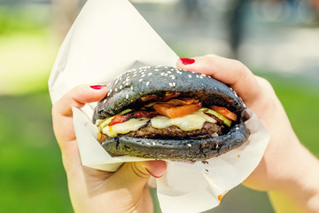 Woman hand holding tasty burger with black bread outdoors
