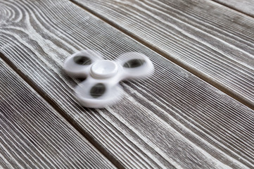 Spinning in motion of a popular white toy spinner on a wooden table. Developing, meditation,...