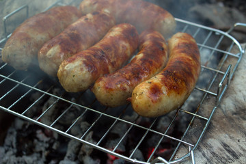 Pork sausage is fried on a charcoal with smoke on the grate