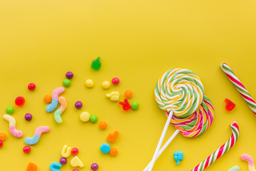 Sweets for birthday including lollipop and drops on yellow background top view copyspace