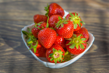 A small white porcelain bowl filled with juicy fresh ripe red strawberries. Textured table top. Fresh strawberries. Strawberries in a Bowl