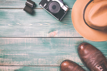Tourism and travel concept. Vintage camera with film, brown shoes and fedora hat on green wooden background. Toned image and free space