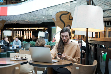 Serious hipster dialing numbers on mobile call to business partner and meet for a coffee break. Student use restaurant wifi connection to check email or surfing social networks and chat friends.