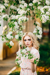 Beautiful young girl standing among the flowering trees. White flowers.