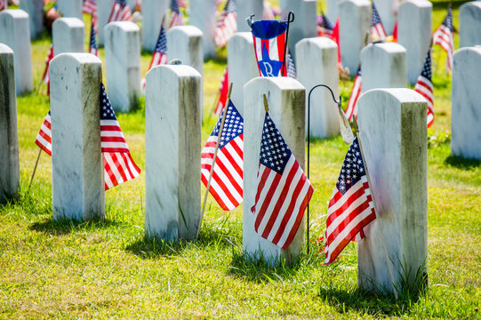 rows of gravestones with American flags in military cemetery