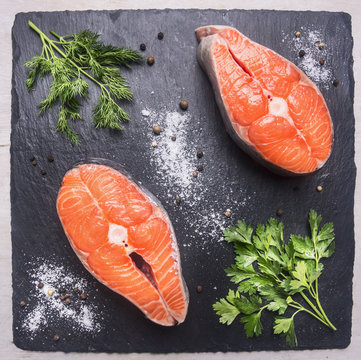 helpful sports foods, cooking two fresh salmon steak with herbs and spices,on a cutting board stone, top view close up