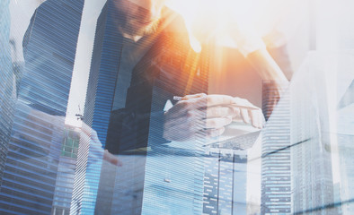Coworking process at a sunny office.Two coworkers using computer at sunny office.Woman pointing on document.Double exposure,skyscraper building blurred background.Horizontal.Flares effect.