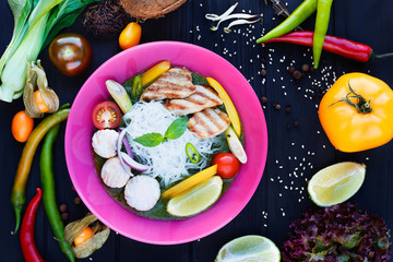 Traditional thai green curry with vegetables, funchoza noodle and chicken, served in bright plate, decorated with soybean sprouts, physalis, coconut, chili peppers, sesame,lime,herbs and spices