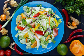 Fresh vegetable thai salad with soybean sprouts on blue plate, decorated with physalis, chili peppers, lime, herbs and spices