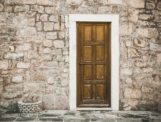 Fototapeta na wymiar Montenegro old town brick wall with wooden door background.
