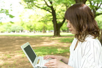 公園でノートパソコンを操作する若い女性　キャンパスライフイメージ