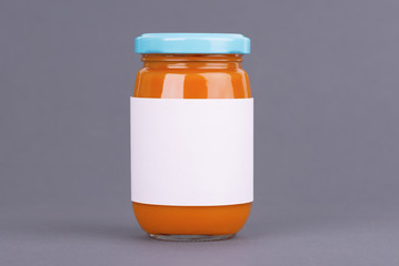 Orange glass jar for baby food bank on grey background. Organic baby food puree. Mock up without template design label.