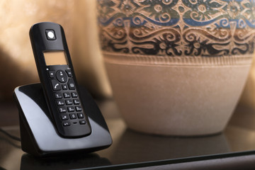 Telephone at hotel room sitting on bedside table with the table lamp.