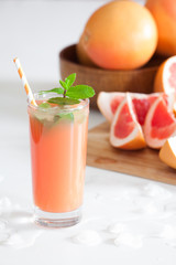 Freshly pressed grapefruit juice with mint leaves and ice on white table close up