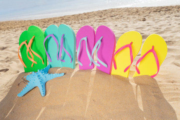 Fototapeta na wymiar Summer beach fun - set of colorful family sandals - green, blue, pink and yellow - in sand on Las Teresitas beach, Tenerife, Canarias