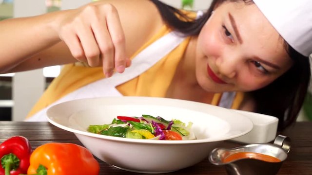  Video footage of a young female chef sprinkling salt into a plate of vegetable salad on the table, shot in the restaurant
