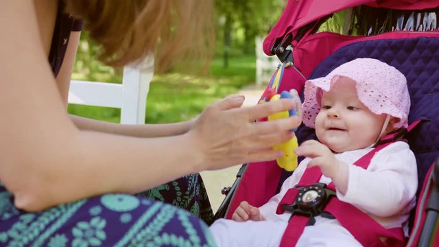 Woman with pram while taking a walk in the park sitting on the bench and playing with her child. Medium shot.