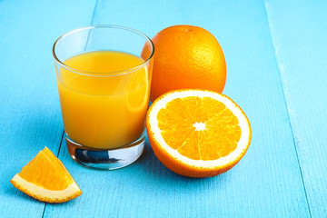 Fresh orange juice in the glass next to the orange slices on blue wooden table