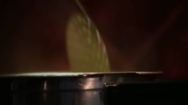 Hand with a slotted spoon is stirring the contents of a pot that is boiling. It is steam coming out of the pot.