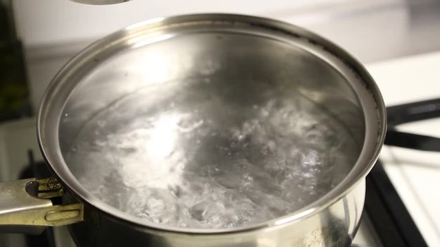 A woman discovers a pot that is on the burner gas cooker, in the pot there boiling water.
