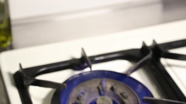A person places a pot of water on a burner gas stove to boil water.