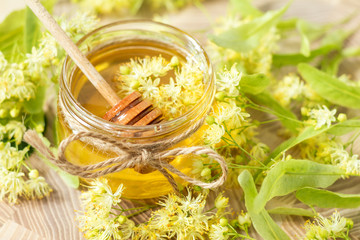 Honey in glass jars with white linden flowers on light wooden background. Shallow depth of field.