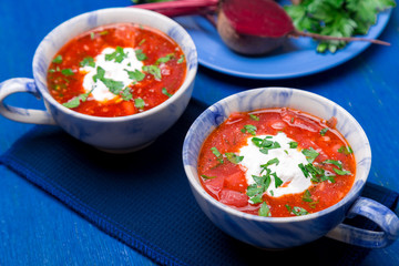 Ukrainian traditional borsch. Russian vegetarian red soup  in blue bowl on blue wooden background.  Borscht, borshch with beet. Two plates. Close up.