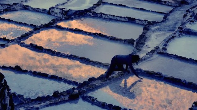 Woman looking her reflection on the salt  ponds during the marvelous sunset. Maras salt terraces in Peru	