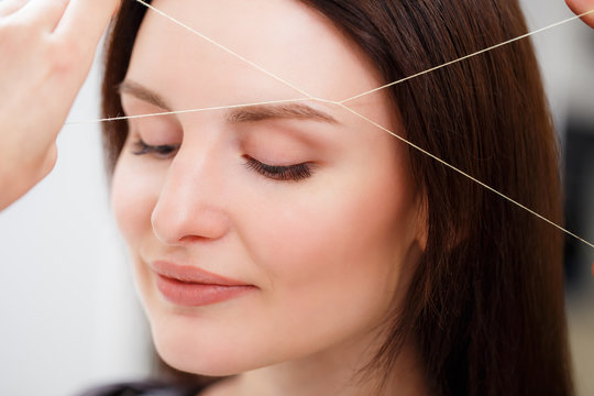 Cosmetologist plucks client eyebrows by thread