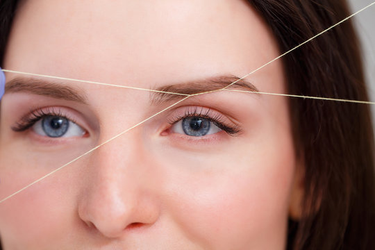 Cosmetologist plucks client eyebrows by thread