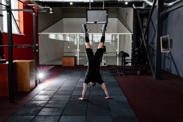 Fototapeta na wymiar Athlete walking on his hands standing upside down in gym. Man doing push ups on his hands. Workout lifestyle concept. Full body length portrait