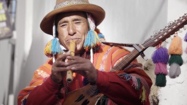 Native quechua man using a colorful handcrafted chullo and a highlander hat, playing flute, typical instrument of Peru on the alleys of Cusco	