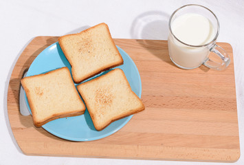 Square toast on a blue plate on a wooden board and a mug of milk