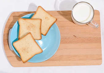 Square toast on a blue plate on a wooden board and a mug of milk