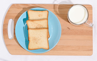 Square toast on a blue plate on a wooden board and a mug of milk