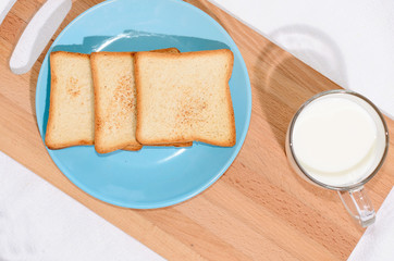 Square toast on a blue plate on a wooden board and a mug of milk