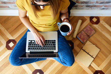 Young woman working on computer sitting on floor with cup of coffee