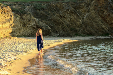 Beautiful young girl in a blue dress on a sandy beach at sunset.