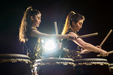 two beautiful asian drummer girl with drumsticks, studio concert shot on a dark background.