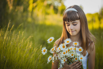 Joyful little girl on a green meadow with a bouquet of chamomiles