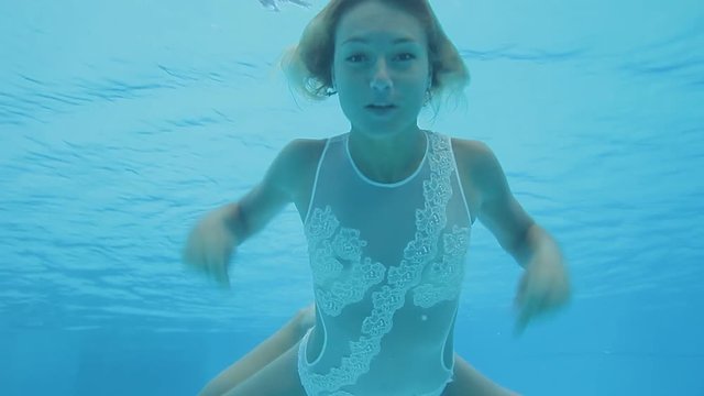 Wonderful woman in a white lace swimsuit swims underwater in a swimming pool