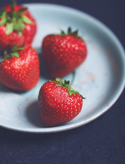 Closeup of fresh strawberries on an old blue vintage plate on dark navy background. Copy space.