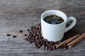 Hot coffee in white mug with splash and coffee beans on wood background
