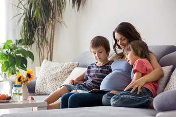 Young pregnant woman, reading a book at home to her two boys